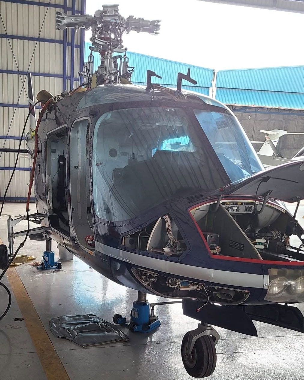 Helicopter on jacks in a hangar with its nose and avionics panels open for maintenance